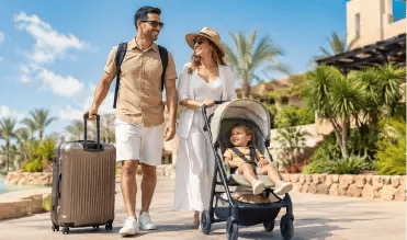 Couple with a baby in a stroller arriving at a resort, the father pulling a rolling suitcase